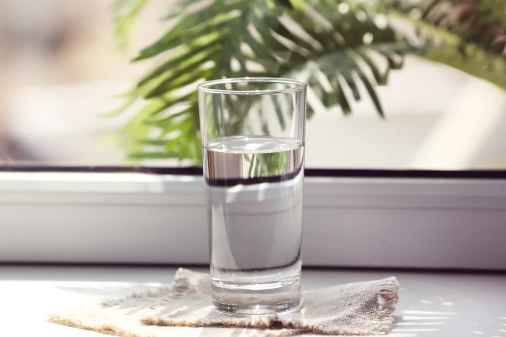 Glass of clean drinking water by a window representing Perth water quality and safe, clear tap water for everyday use.