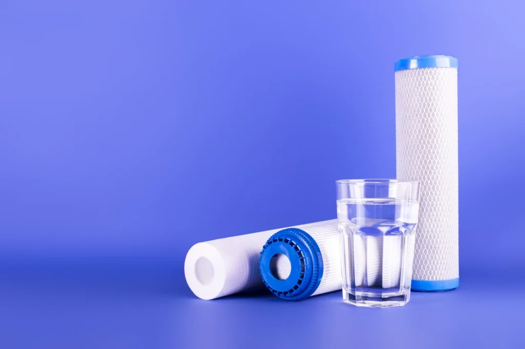Water filter cartridges and clean glass of water representing filter replacement for maintaining safe and effective water filtration.